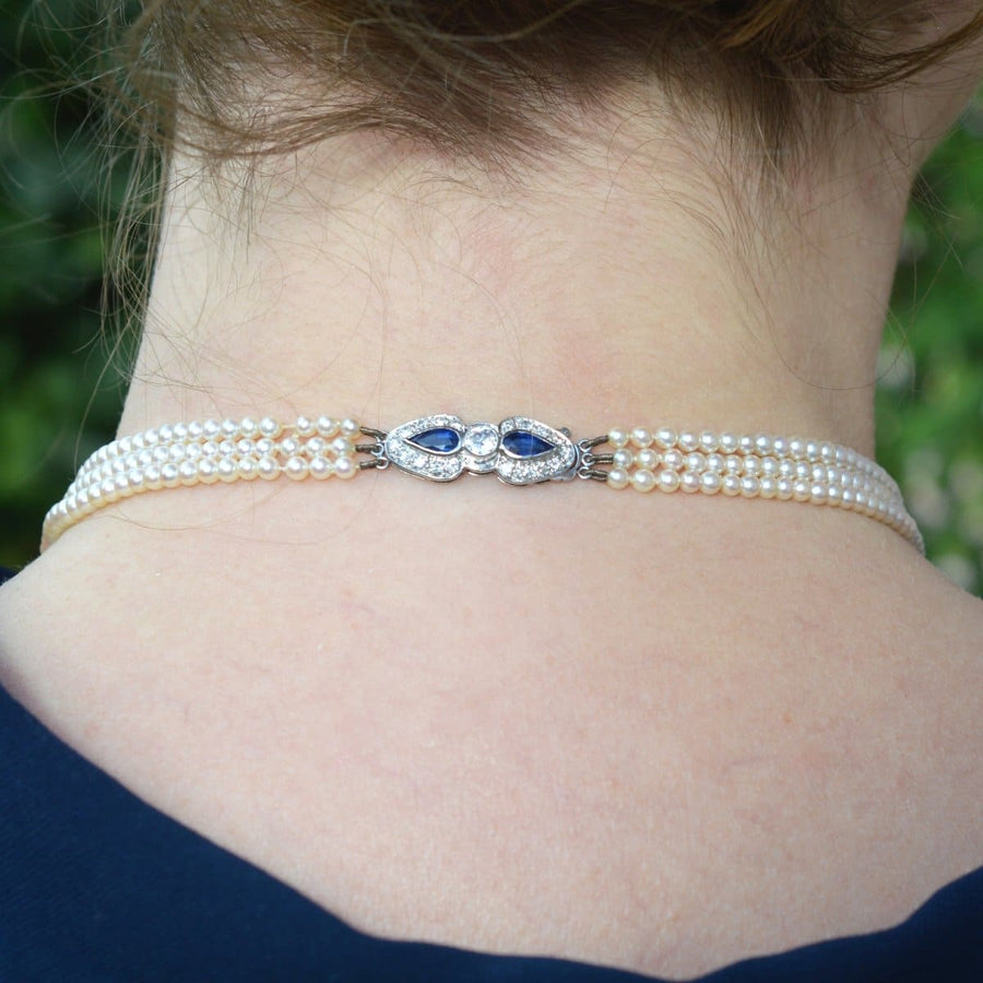1940s cultured pearl triple strand necklace with sapphire and diamond clasp, worn on the neck.