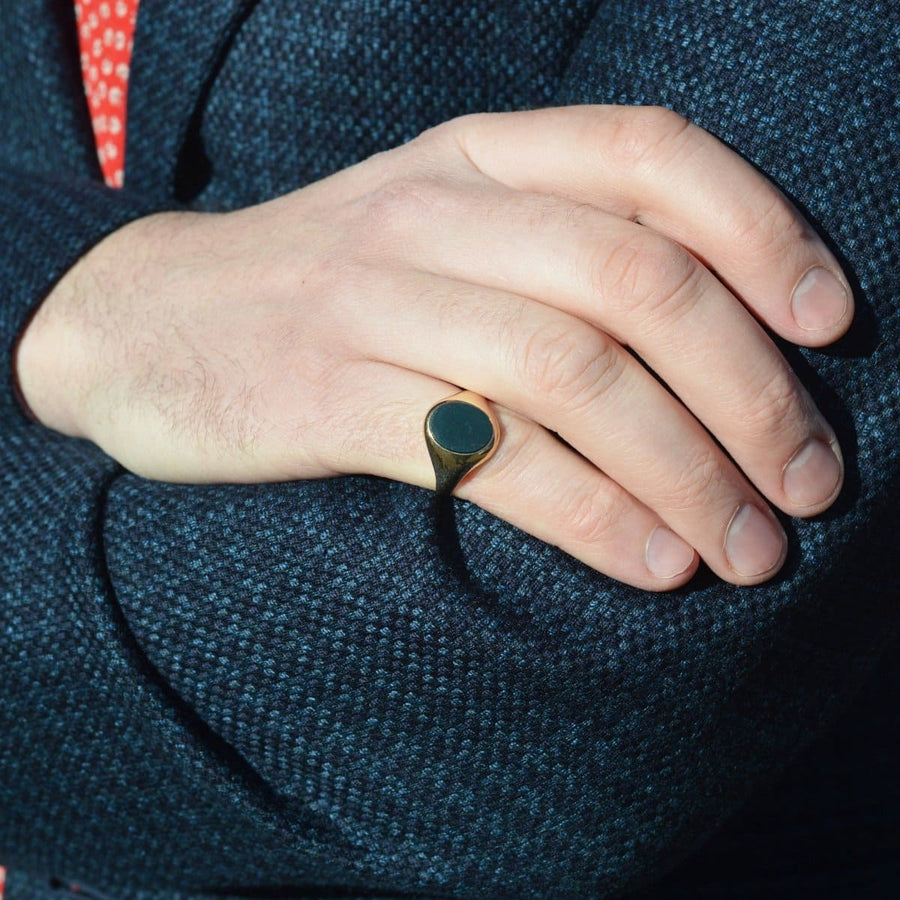1960s 9ct gold signet ring with bloodstone worn on a hand against a stylish jacket background.