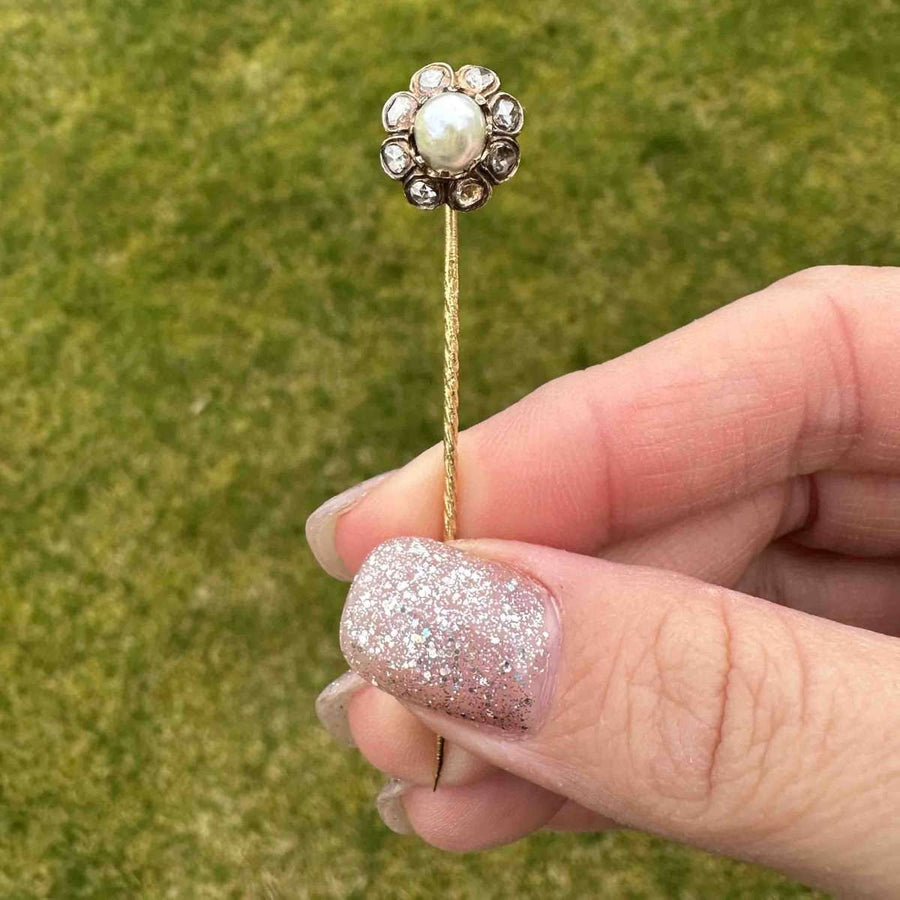 19th Century 18ct gold tie pin showcasing a natural pearl surrounded by rose cut diamonds, held by a hand with glittery nails.