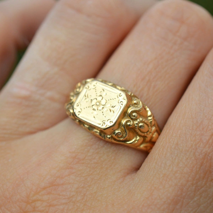 Antique French 18ct gold ring with engraved floral design and swirled shoulders, showcased on a hand.