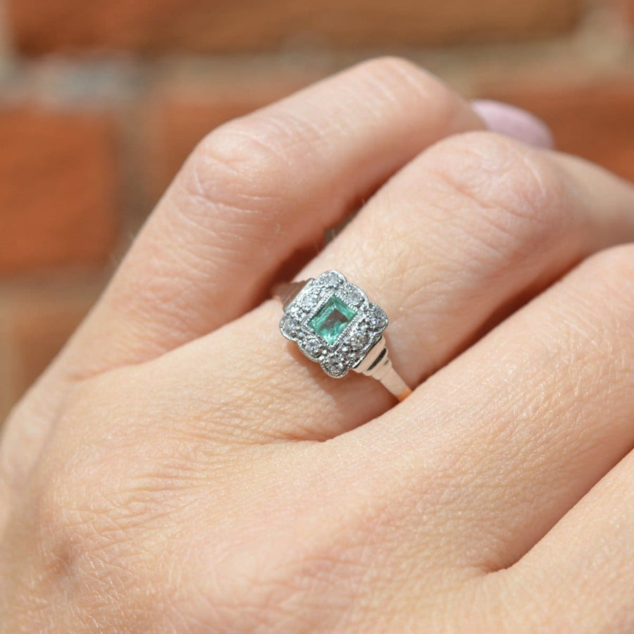 Art Deco 18ct gold and platinum ring featuring an emerald surrounded by diamonds in a millegrain setting.