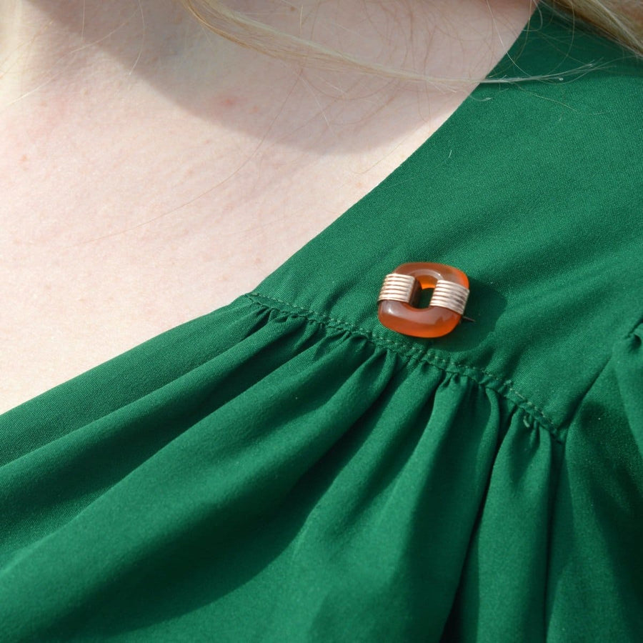 Detail of a stylish Art Deco 9ct gold carnelian agate brooch on a green dress, perfect for both men and women.