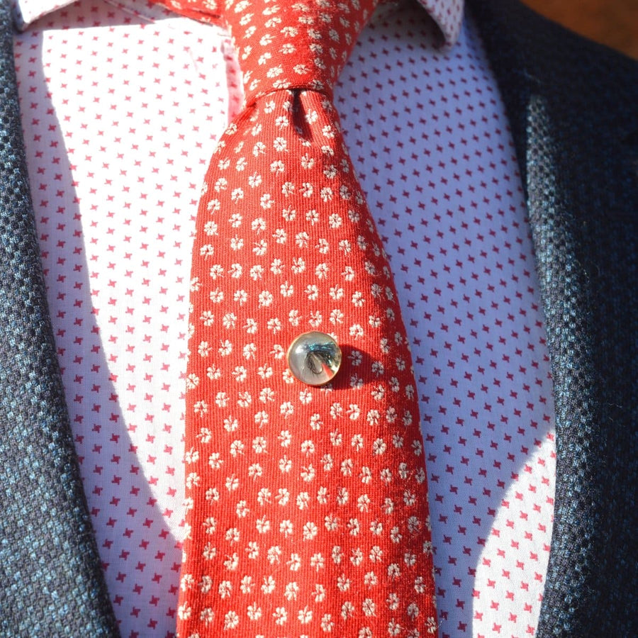 Close-up of a red patterned tie with a silver tie pin, worn over a white and red patterned shirt.
