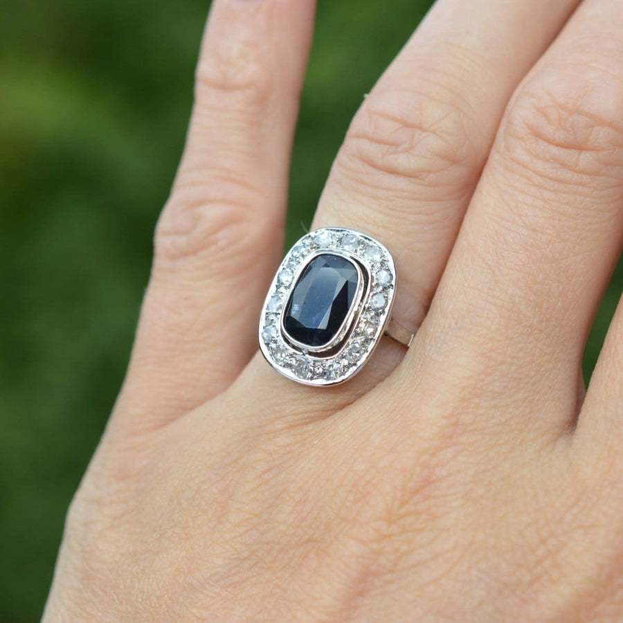 Art Deco platinum ring featuring a dark sapphire surrounded by diamonds, perfect for an engagement or special occasion.