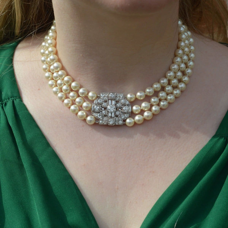 Art Deco platinum and diamond brooch on a pearl necklace, showcasing a bold geometric design and luxurious elegance.