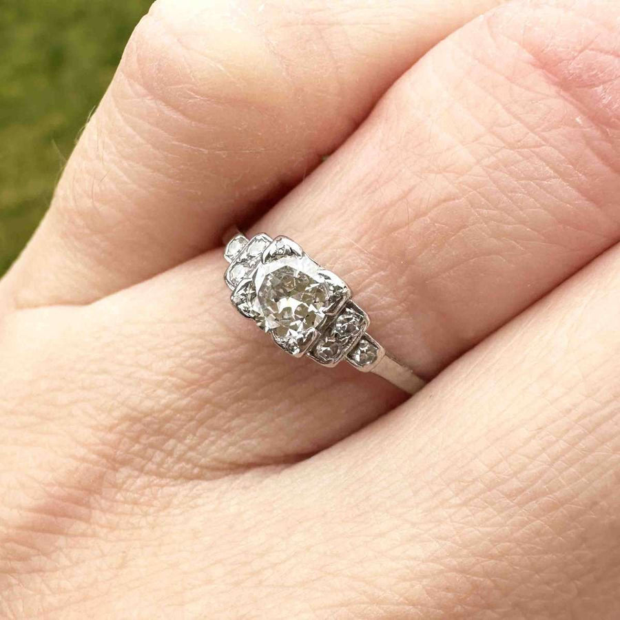 Art Deco platinum diamond solitaire ring with step-like diamond shoulders on a hand.