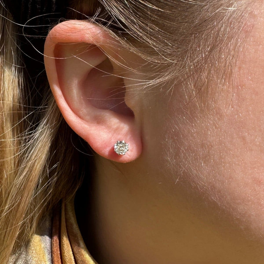 Close-up of a person's ear wearing Art Deco platinum diamond stud earrings with a sparkling design.