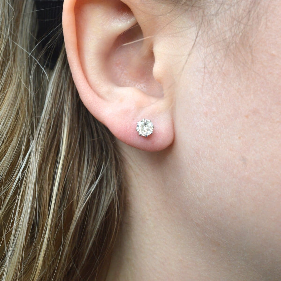 Close-up of a person wearing Art Deco platinum diamond stud earrings, showcasing half-carat diamond brilliance.