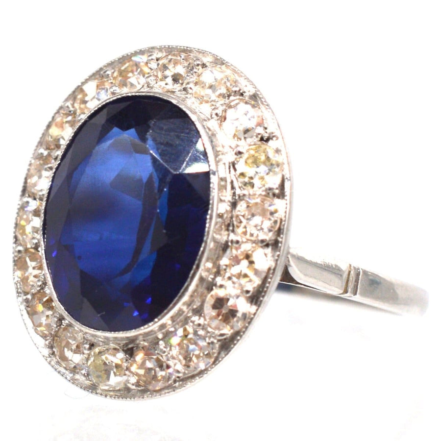 Art Deco platinum ring featuring a synthetic sapphire surrounded by diamond cluster accents.