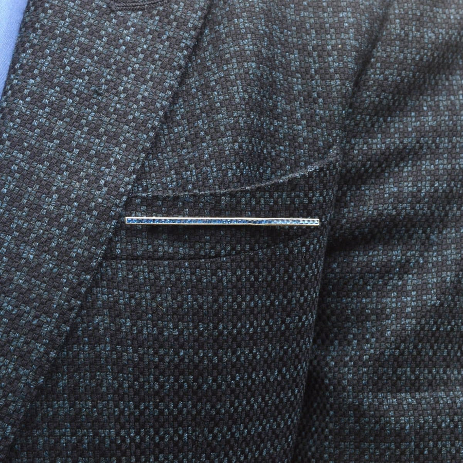 Art Deco silver bar brooch with blue paste stones on a dark patterned suit jacket.