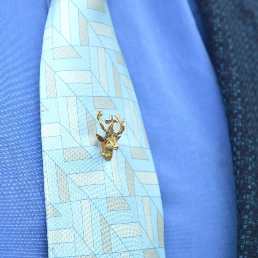 14ct gold and rose diamond tie pin featuring the St. Hubertus stag, adorns a patterned blue tie.