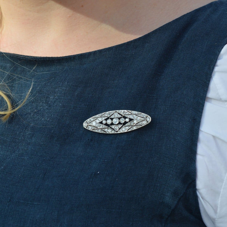 Early 20th century French platinum and gold diamond brooch worn on a blue dress, showcasing geometric design and fine craftsmanship.