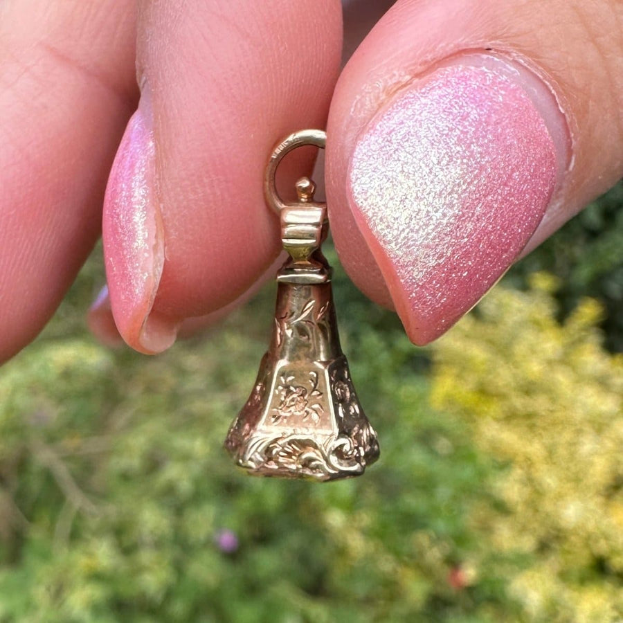 Early Victorian gold cased bell charm held between fingers, featuring intricate floral designs.