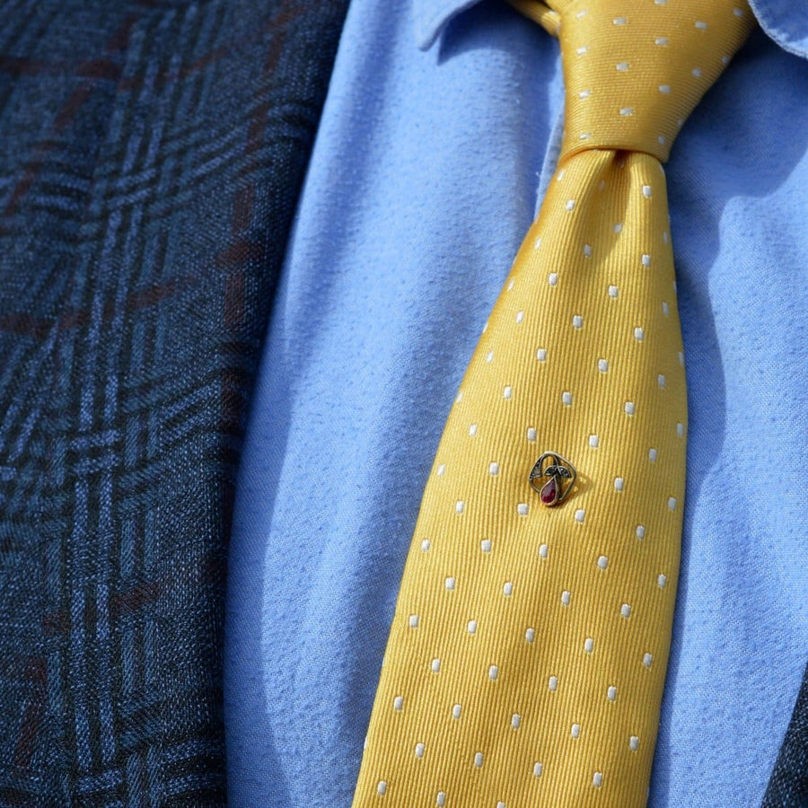 Close-up of a yellow polka dot tie with a decorative tie pin, worn with a patterned blazer.