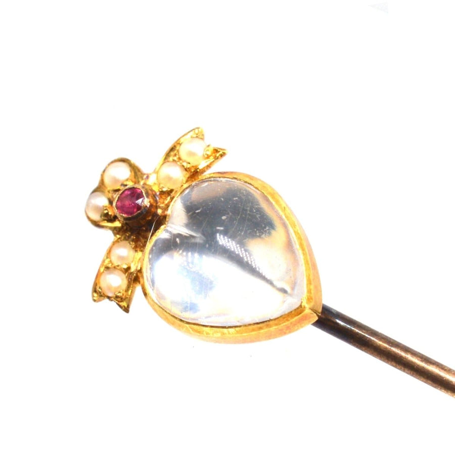 Edwardian 15ct gold bow tie pin featuring a moonstone heart, ruby, and seed pearls for elegance and charm.
