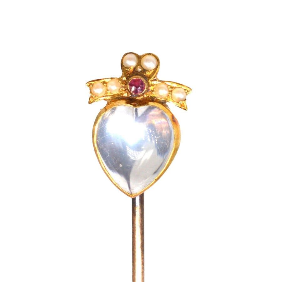Edwardian gold moonstone heart pin with ruby and seed pearl bow tie design, symbolizing love and good luck.