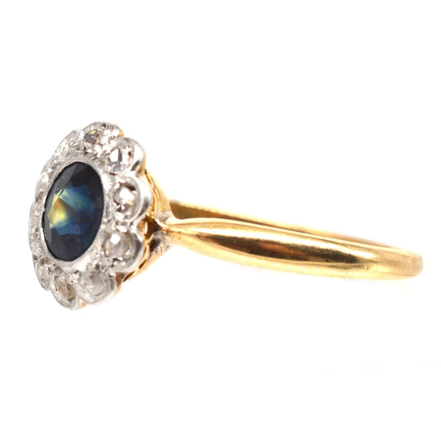 Edwardian 18ct gold cluster ring featuring a teal sapphire surrounded by brilliant diamonds.