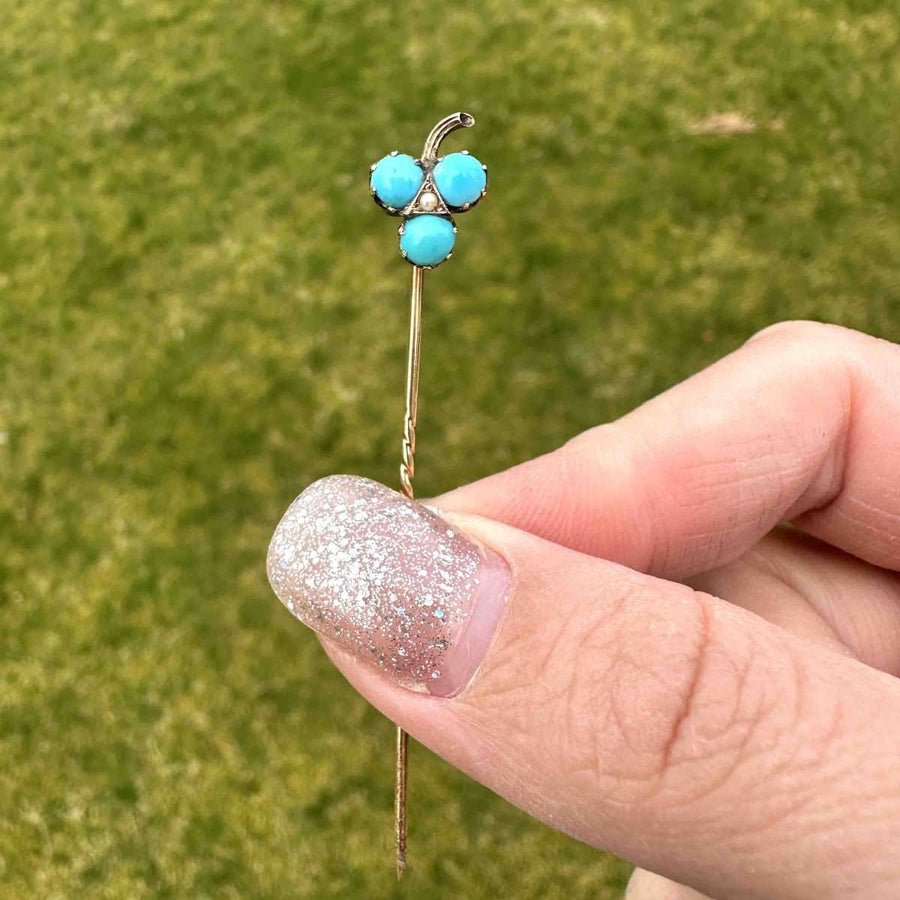 Edwardian 9ct gold shamrock tie pin with turquoise and pearl, held in hand against green grass.
