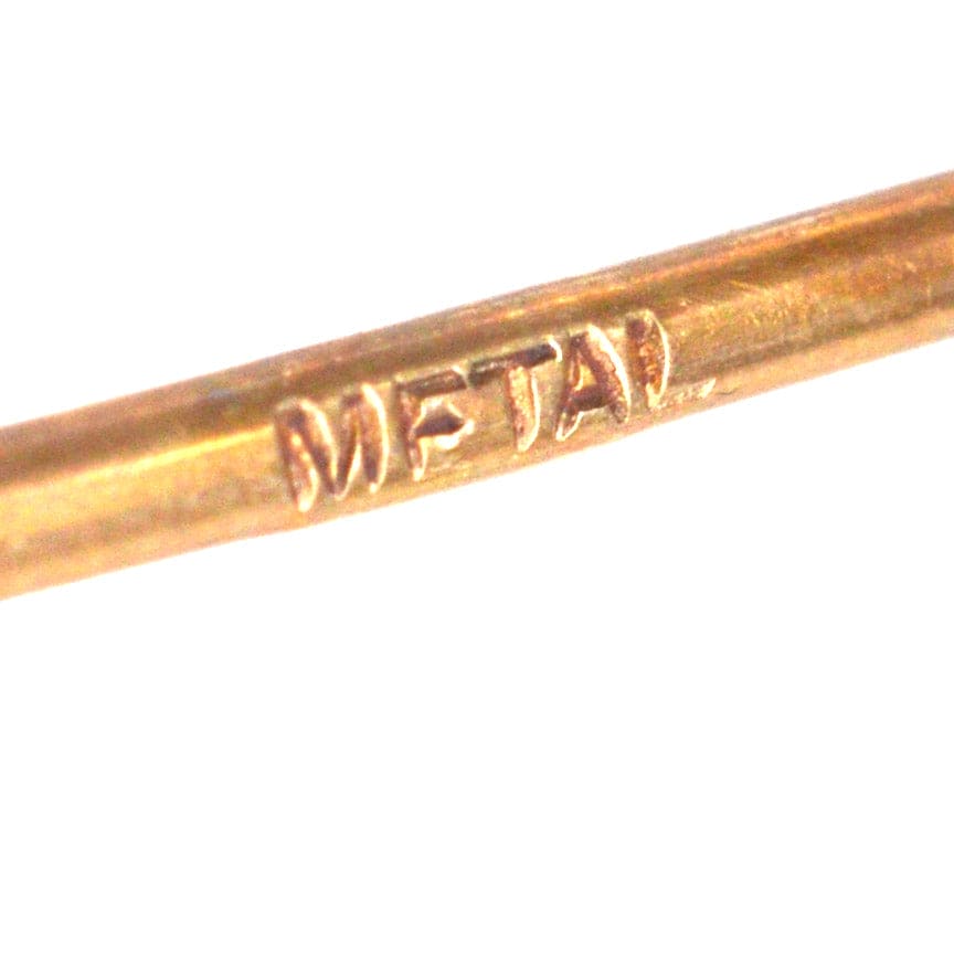Close-up of a metal tie pin with the word 'METAL' engraved on it.