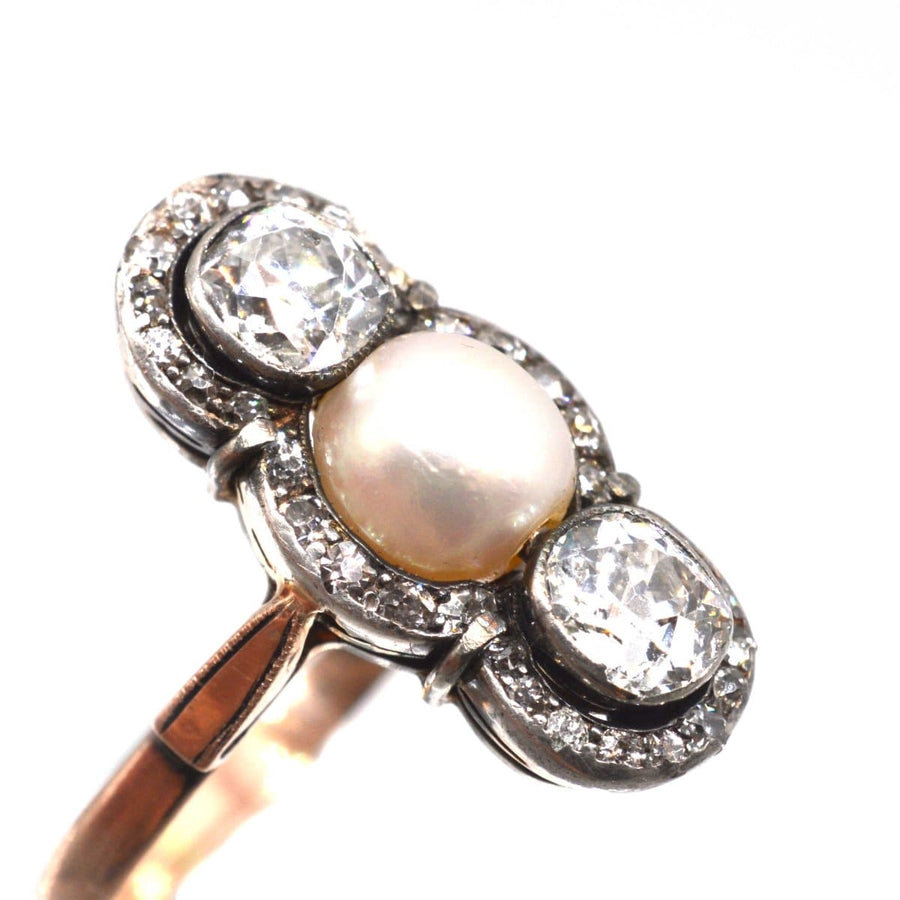 Edwardian silver and gold ring featuring a central natural pearl and two old mine cut diamonds with decorative accents.