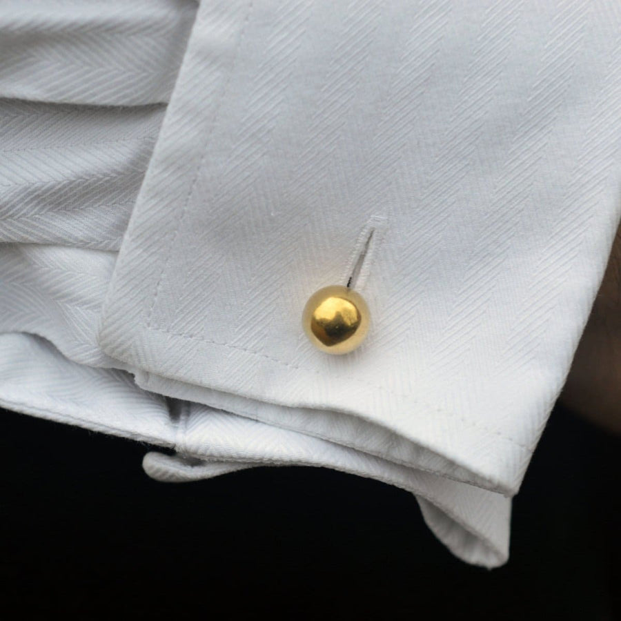Close-up of a cufflink featuring a gold ball on a white dress shirt cuff, showcasing elegance and style.