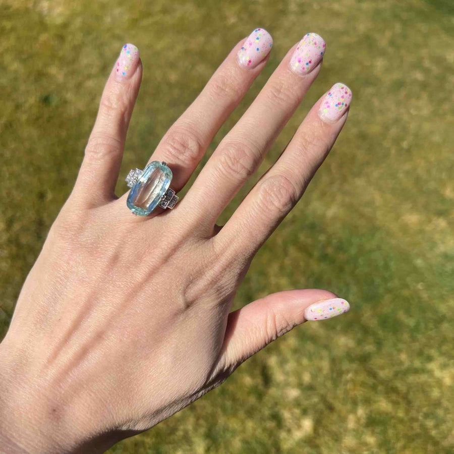 Fashionable hand showcasing a vintage platinum ring with a large aquamarine and diamond accents on a sunny background.