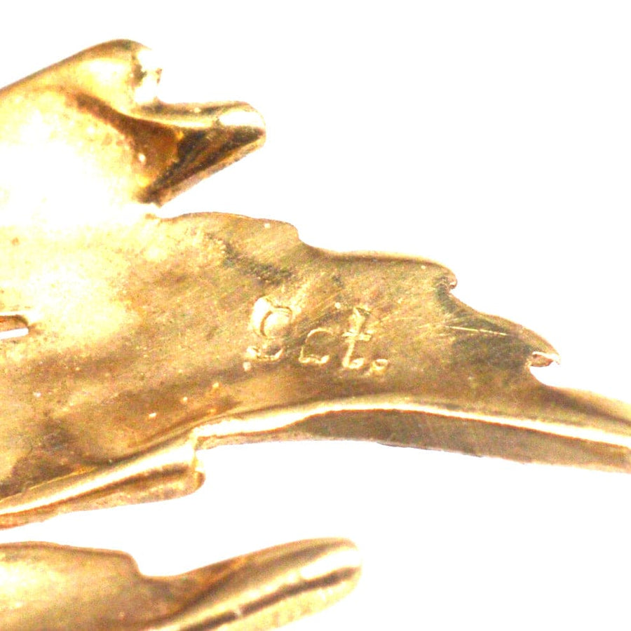Close-up of a mid-century gold brooch featuring hallmarks indicating quality, with a naturalistic floral design.