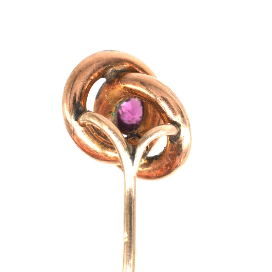 Victorian gold knot tie pin featuring a central garnet gemstone, symbolizing the lover's knot, circa 1880s.