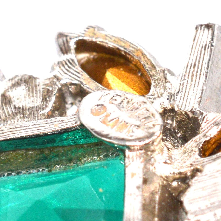 Close-up of vintage Kenneth Lane clip-on earrings showcasing green paste stone and signature tag.