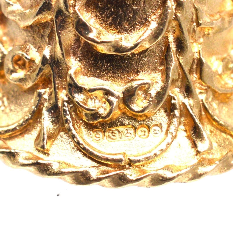 Close-up of hallmarked 9ct gold vintage wedding ring charm showing scroll details and manufacturer mark.