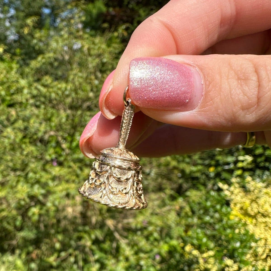 Hand holding a vintage 9ct gold wedding ring bell charm pendant with intricate scrolls, perfect for wedding gifts or collectors.