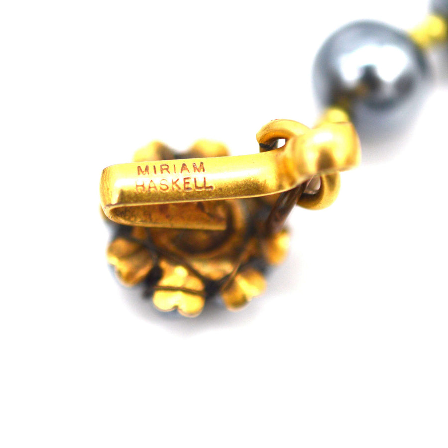 Close-up of Miriam Haskell gold gilt clasp showcasing signature, with black pearl necklace in the background.