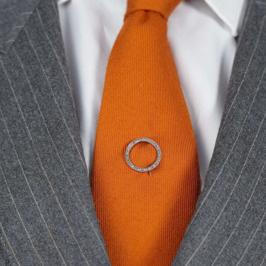 Art Deco 15ct gold and platinum rose diamond round circle brooch on an orange tie, showcased in a stylish suit.