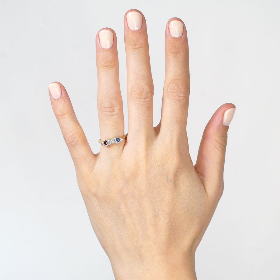 Art Deco gold and platinum ring featuring an oval ruby, sapphire, and sparkling diamonds on a hand.
