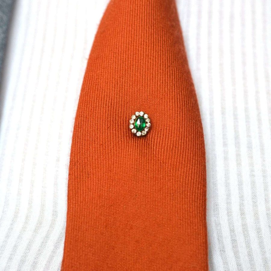 Art Deco green emerald and white paste tie pin on an orange silk tie, adding vintage elegance to formal attire.