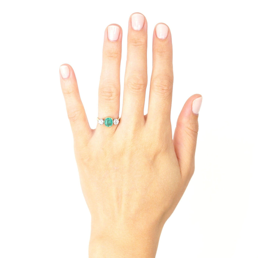 Art Deco platinum and 18ct gold emerald and diamond three stone ring worn on a hand, showcasing its elegant design.
