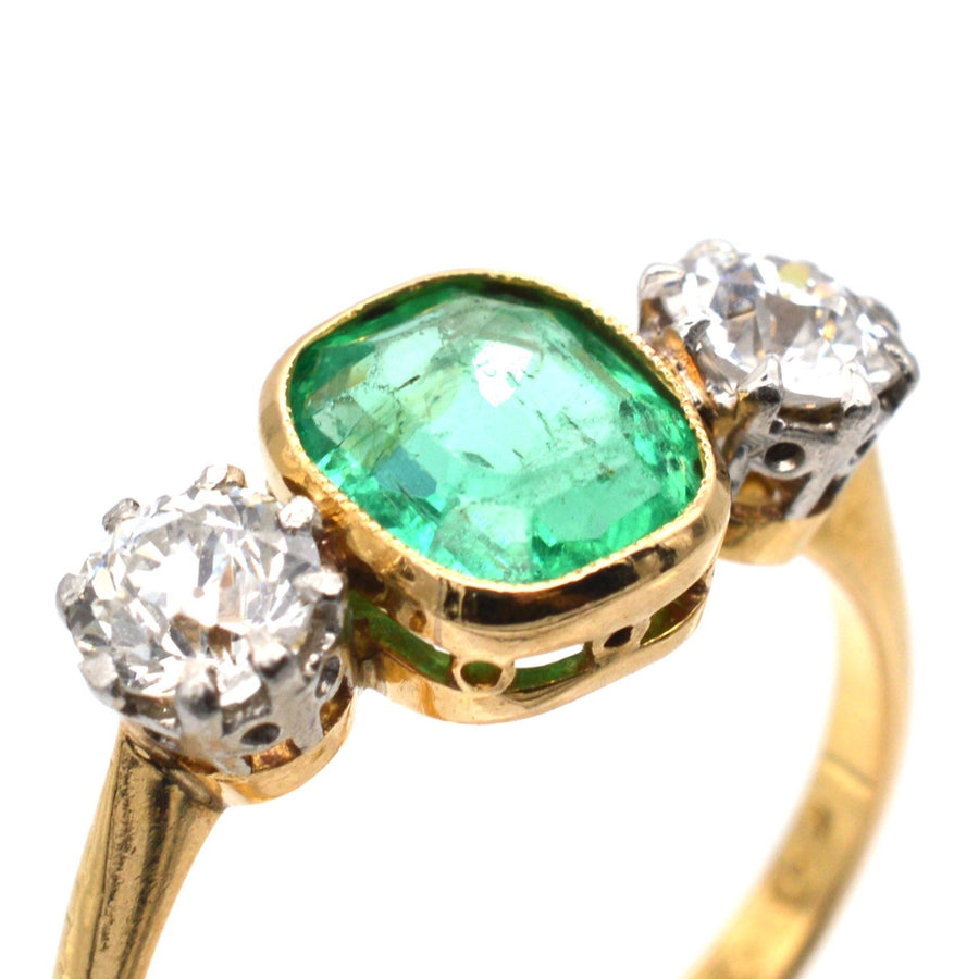 Art Deco three stone ring featuring a vibrant emerald center with diamond accents in gold and platinum setting.