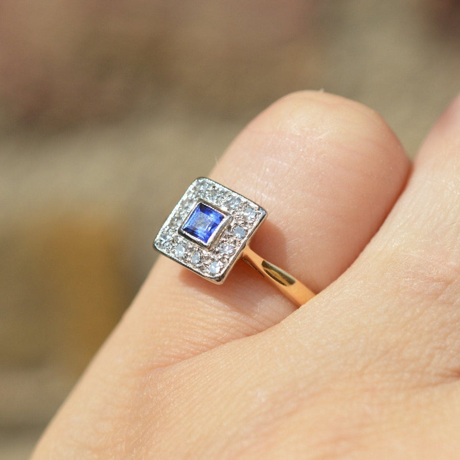 Art Deco platinum and gold sapphire diamond cluster ring on hand, showcasing vibrant blue sapphire and intricate geometric design.