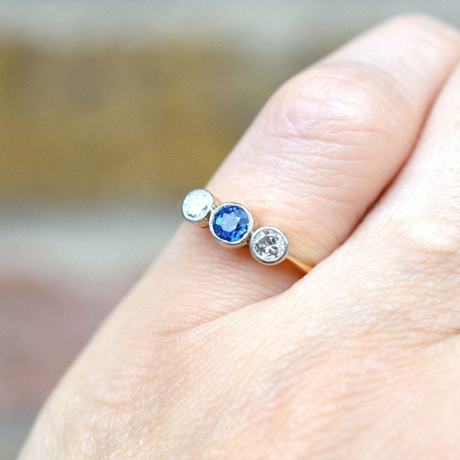 Art Deco three stone sapphire and diamond bezel ring on hand, showcasing vibrant blue sapphire and sparkling diamonds.