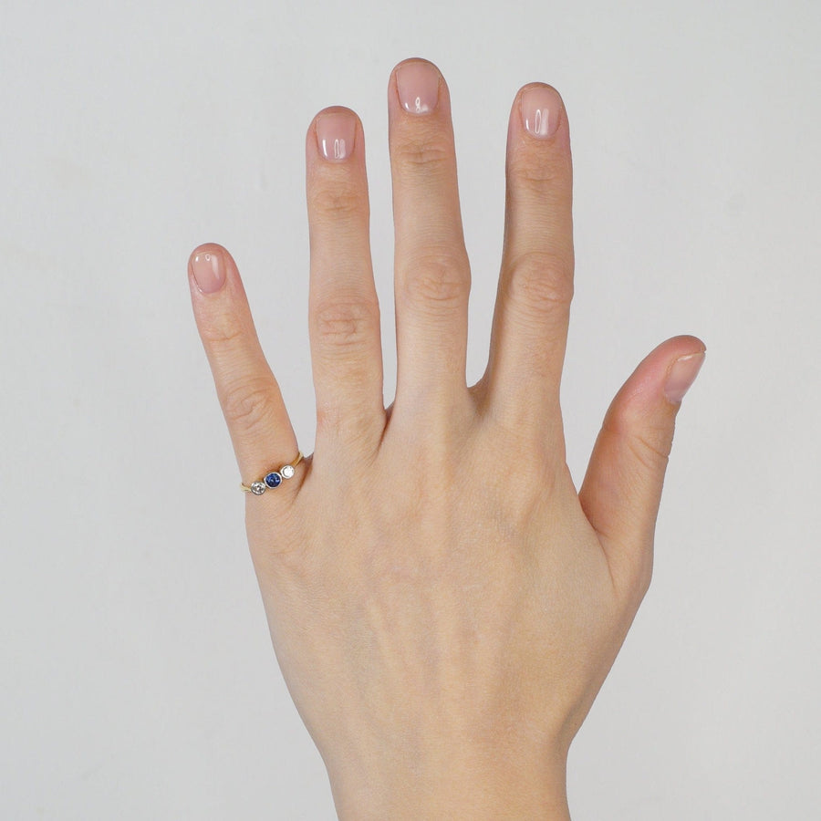 Art Deco gold three stone sapphire and diamond bezel ring displayed on a hand.