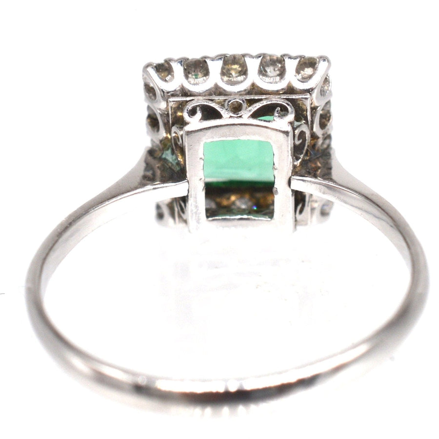 Art Deco platinum rectangular emerald and diamond cluster ring with engraved shoulders and vibrant green emerald