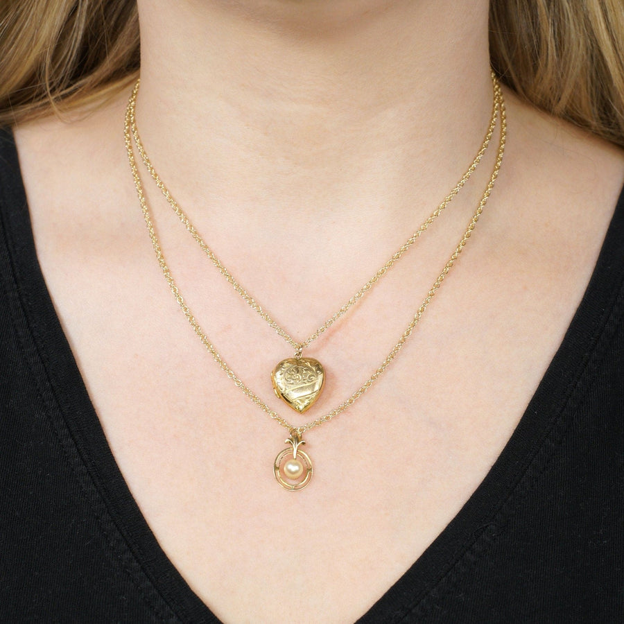 Layered gold heart and circle necklaces worn together on a black shirt.