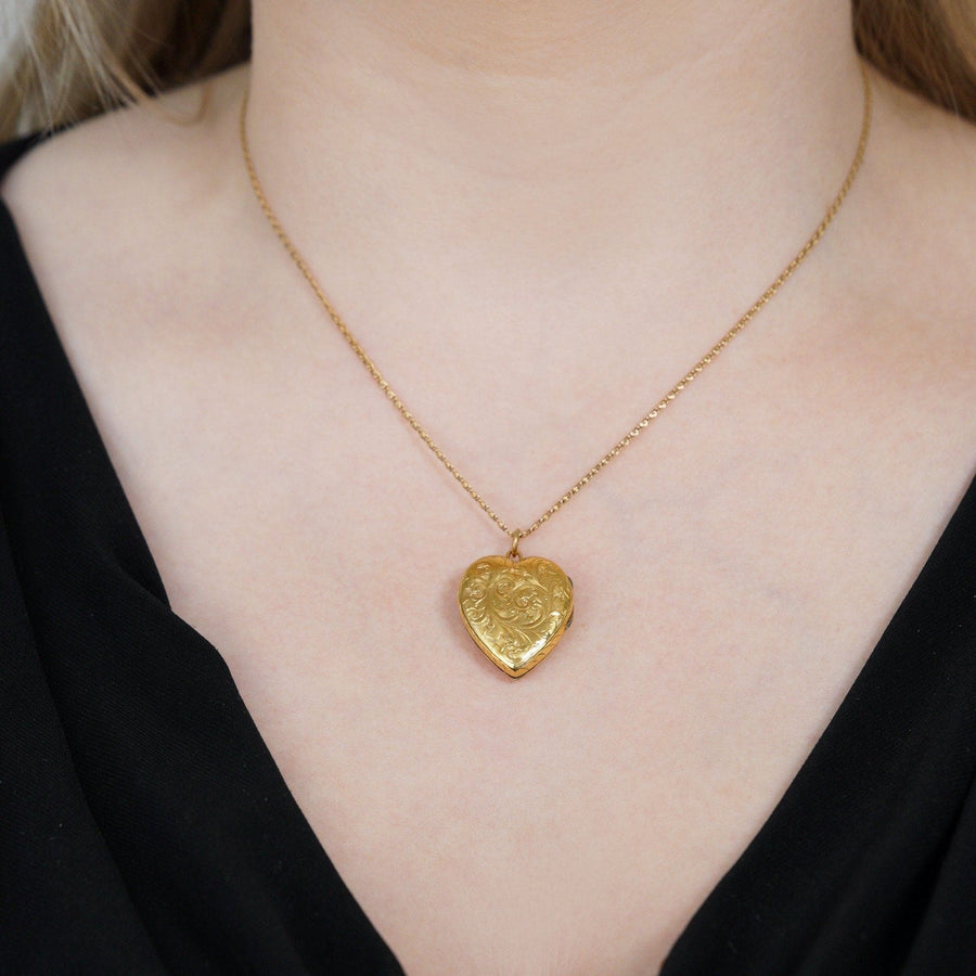Edwardian 9ct gold heart locket pendant worn on a woman's neck, showcasing intricate engravings and a stylish design.