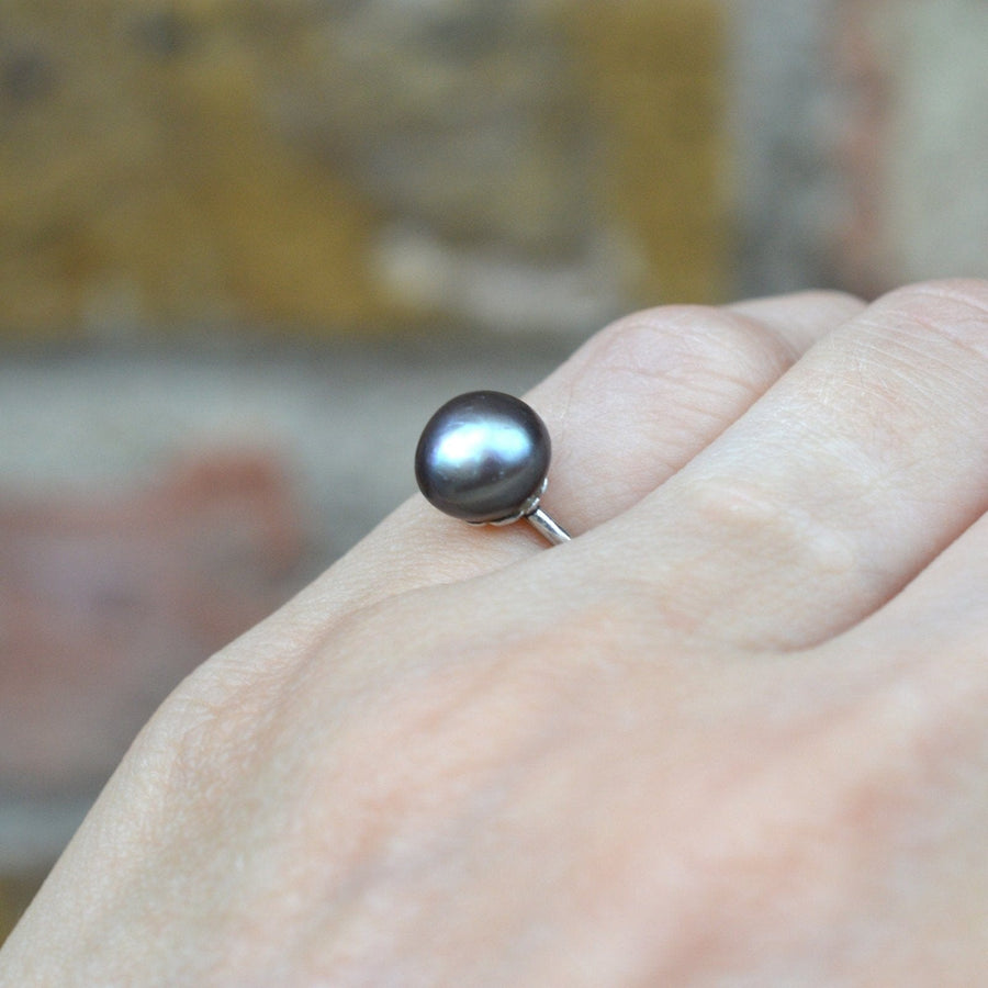 Edwardian platinum ring featuring a natural black saltwater pearl on a hand against a blurred background.