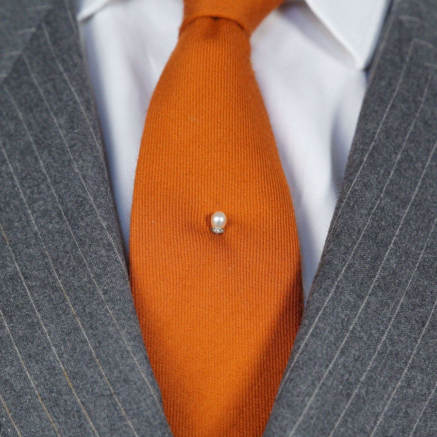 Edwardian platinum tie pin featuring a natural pearl and diamonds against an orange silk tie.