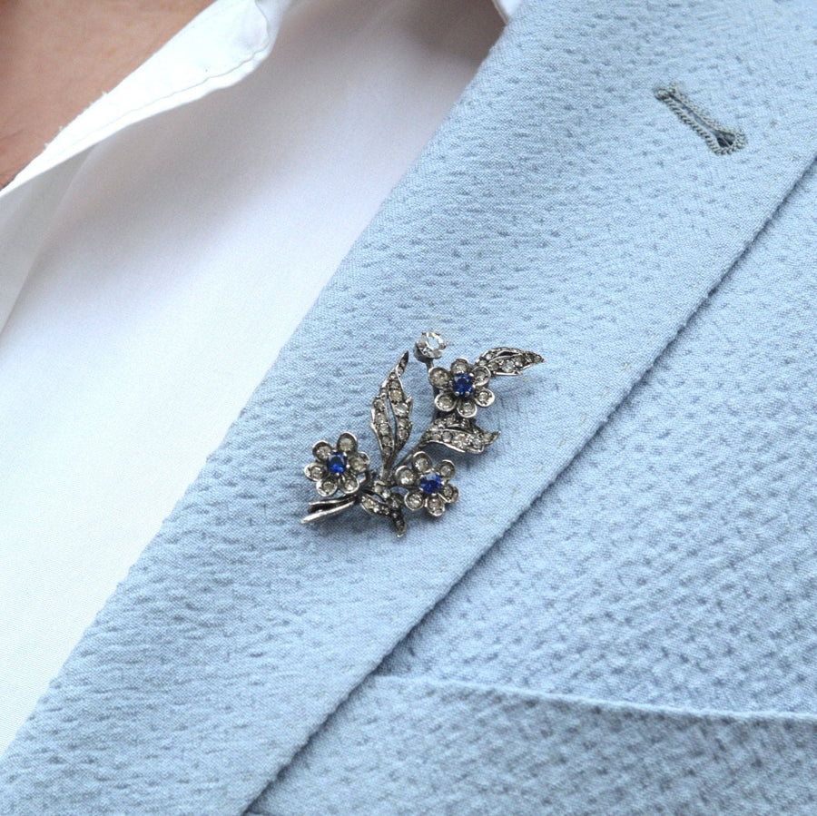 Edwardian silver brooch with blue sapphires and white paste, styled on a light blue blazer lapel.