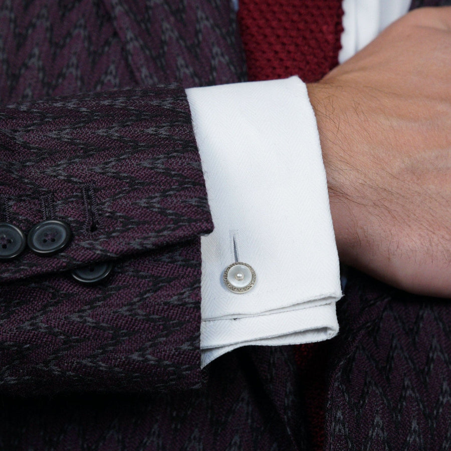 Elegant cufflinks featuring a pearl and diamond design worn on a stylish suit sleeve.