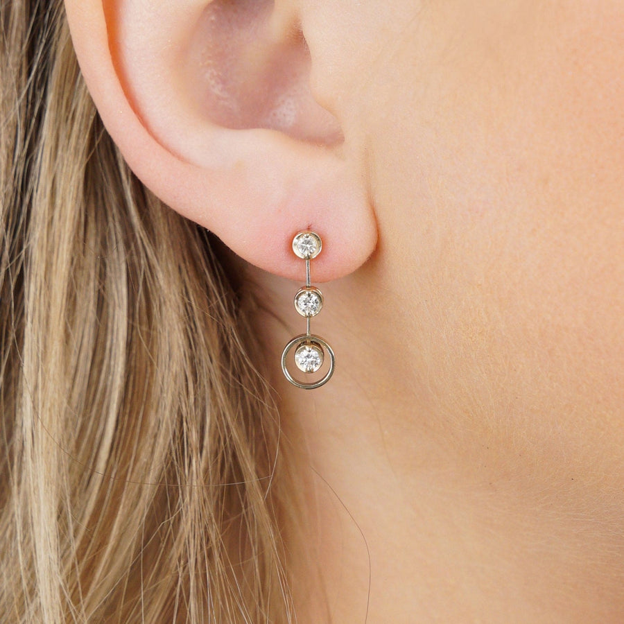 Modern 18ct gold three stone diamond drop earrings showcasing bright white diamonds and contemporary design.