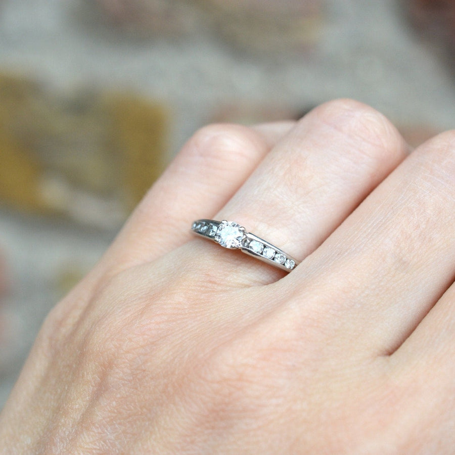 Modern 18ct white gold solitaire ring with diamond shoulders on a hand.