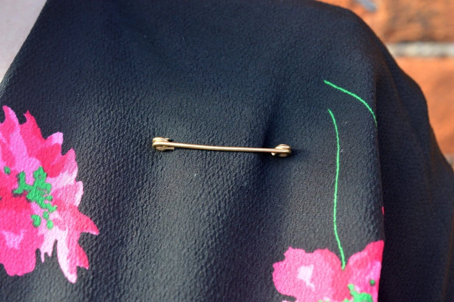 Vintage 9ct gold stock pin brooch on floral fabric, showcasing its elegant design and historical significance.